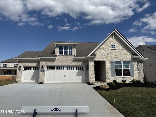 view of front facade featuring roof with shingles, driveway, stone siding, a front yard, and a garage