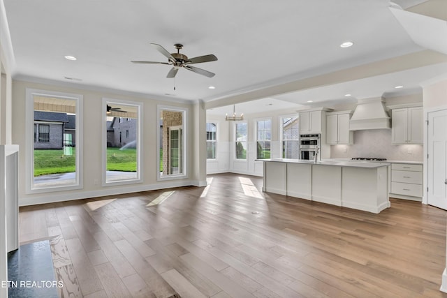 unfurnished living room with ceiling fan with notable chandelier, light wood finished floors, ornamental molding, and recessed lighting