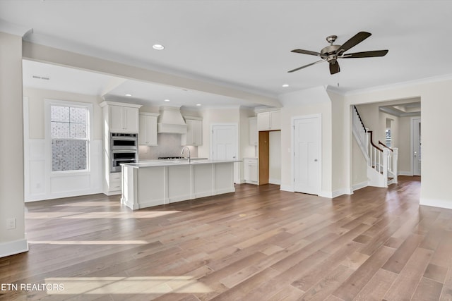 unfurnished living room featuring light wood-type flooring, ceiling fan, a sink, and stairway
