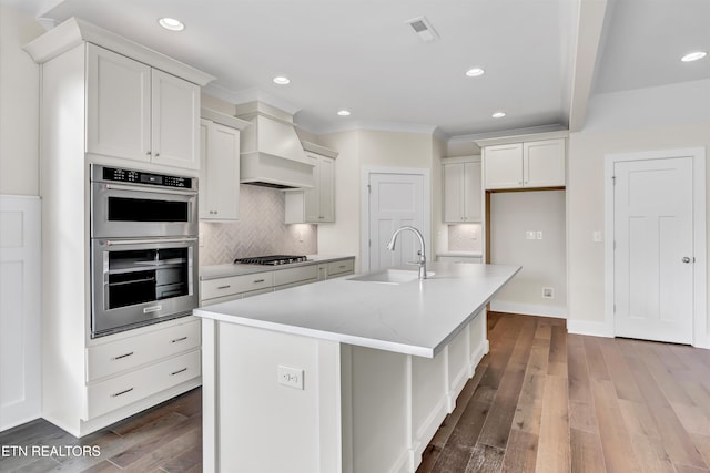 kitchen with ornamental molding, visible vents, a sink, stainless steel appliances, and premium range hood