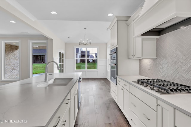 kitchen with an inviting chandelier, premium range hood, decorative backsplash, stainless steel appliances, and a sink