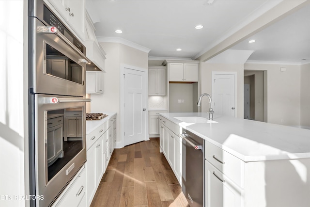 kitchen with ornamental molding, white cabinets, appliances with stainless steel finishes, light countertops, and hardwood / wood-style flooring