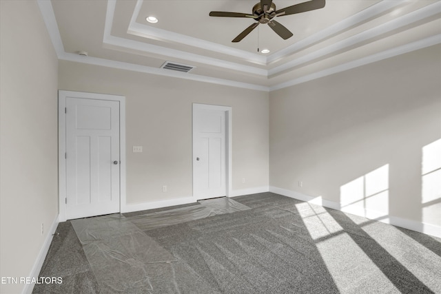spare room with dark colored carpet, visible vents, a tray ceiling, and ceiling fan