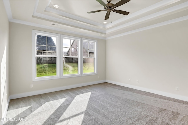 carpeted spare room with a tray ceiling, ceiling fan, baseboards, and visible vents
