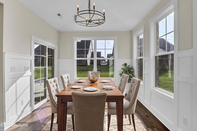 dining area featuring dark wood-type flooring, a notable chandelier, wainscoting, and visible vents