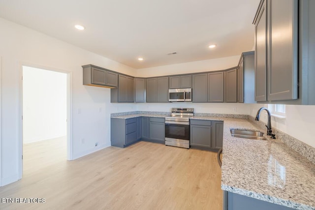 kitchen featuring sink, gray cabinets, light stone countertops, appliances with stainless steel finishes, and light hardwood / wood-style floors