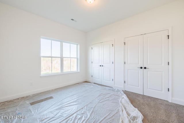 unfurnished bedroom with light carpet and two closets