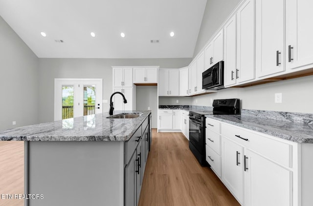 kitchen with lofted ceiling, sink, a center island with sink, white cabinetry, and black appliances