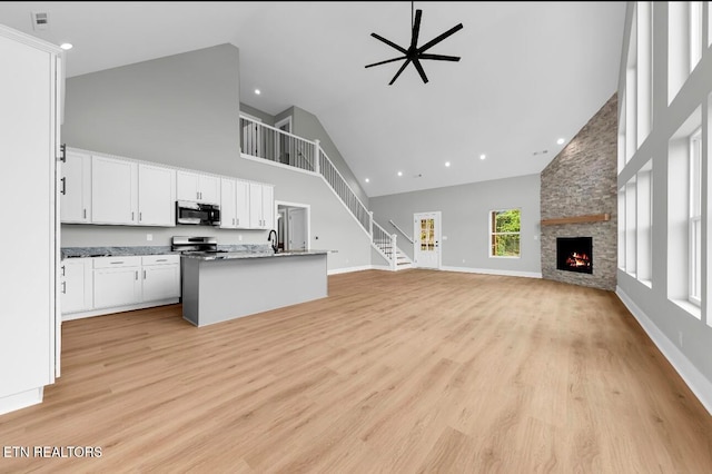 kitchen featuring light wood-type flooring, a stone fireplace, high vaulted ceiling, appliances with stainless steel finishes, and white cabinetry