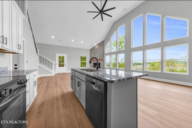 kitchen with an island with sink, black appliances, a wealth of natural light, dark stone counters, and white cabinetry