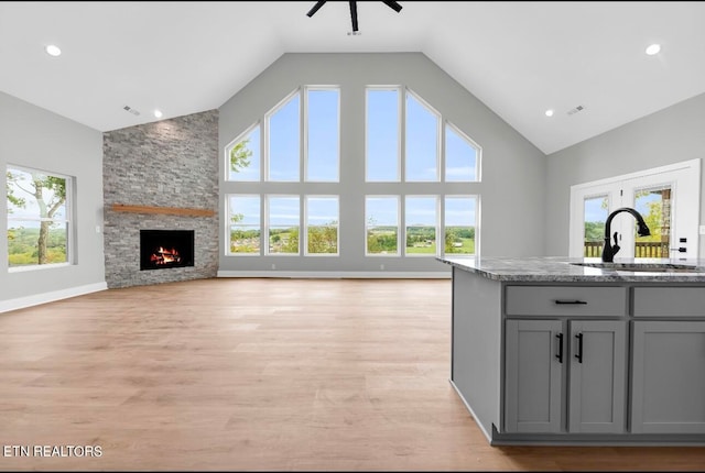 kitchen with sink, stone counters, gray cabinets, a fireplace, and light wood-type flooring