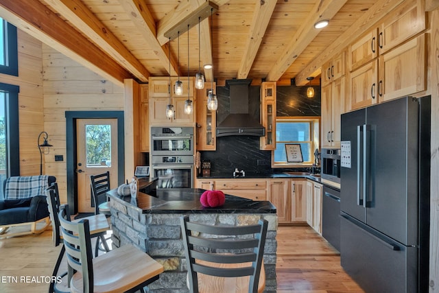 kitchen with decorative light fixtures, wooden walls, appliances with stainless steel finishes, light brown cabinetry, and light wood-type flooring