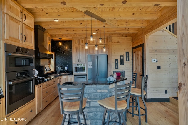 kitchen with pendant lighting, wood walls, wall chimney exhaust hood, appliances with stainless steel finishes, and light wood-type flooring