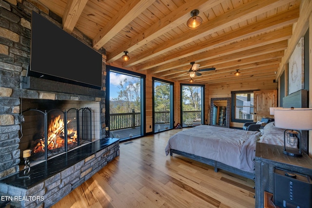 bedroom featuring wooden walls, wooden ceiling, a fireplace, light hardwood / wood-style flooring, and beam ceiling