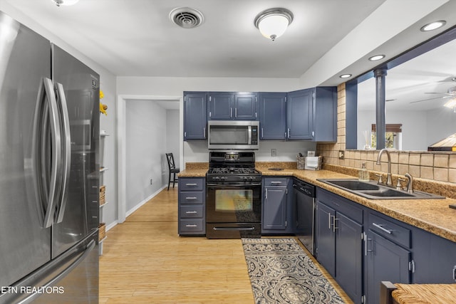 kitchen featuring appliances with stainless steel finishes, decorative columns, blue cabinetry, light hardwood / wood-style flooring, and sink