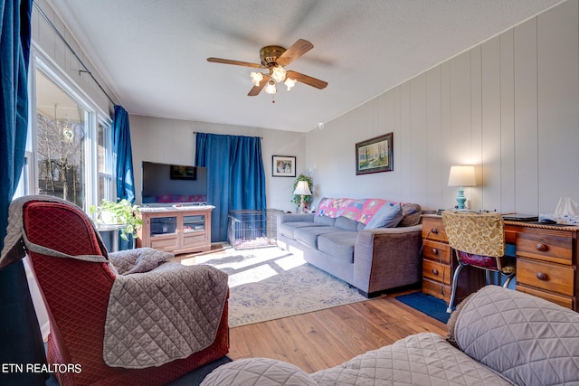 living room with ceiling fan, a textured ceiling, light wood-type flooring, and wooden walls