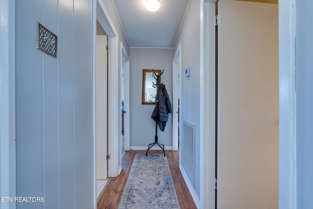 hallway with wooden walls, light hardwood / wood-style floors, and a textured ceiling