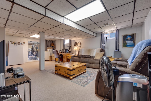 carpeted living room featuring a drop ceiling and a wood stove