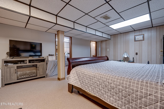 bedroom with light colored carpet, a drop ceiling, and wood walls