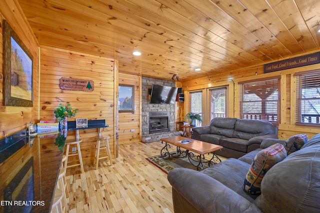 living room featuring wooden walls, a stone fireplace, wood ceiling, and light hardwood / wood-style flooring