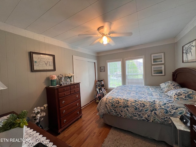 bedroom featuring ceiling fan, crown molding, wooden walls, and light hardwood / wood-style flooring