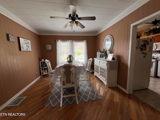 dining area with wooden walls, ceiling fan, ornamental molding, and hardwood / wood-style flooring