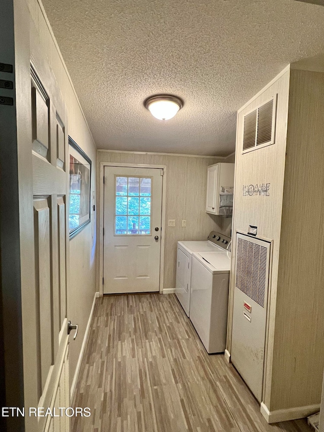 laundry room with separate washer and dryer, cabinets, light wood-type flooring, and a textured ceiling