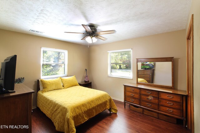 bedroom featuring a textured ceiling, dark hardwood / wood-style floors, multiple windows, and ceiling fan