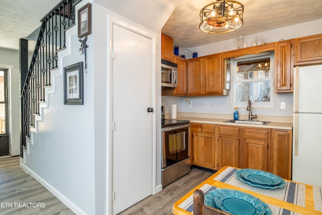 kitchen with a textured ceiling, sink, light hardwood / wood-style floors, decorative light fixtures, and stainless steel appliances