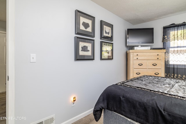 bedroom featuring a textured ceiling, hardwood / wood-style flooring, and vaulted ceiling