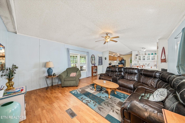 living room featuring vaulted ceiling, a textured ceiling, light hardwood / wood-style floors, and ceiling fan