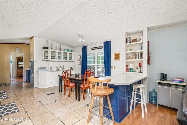 kitchen with lofted ceiling, white cabinets, a kitchen breakfast bar, a textured ceiling, and light hardwood / wood-style floors