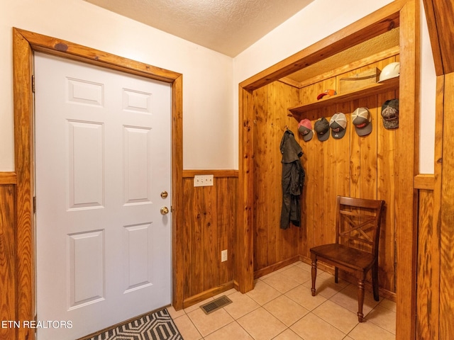 mudroom with wood walls, light tile patterned floors, and a textured ceiling