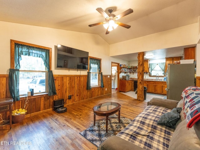 living room with lofted ceiling, wooden walls, ceiling fan, and light hardwood / wood-style flooring