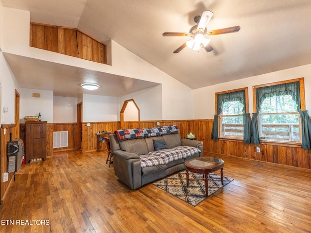 living room featuring ceiling fan, hardwood / wood-style flooring, wood walls, and vaulted ceiling