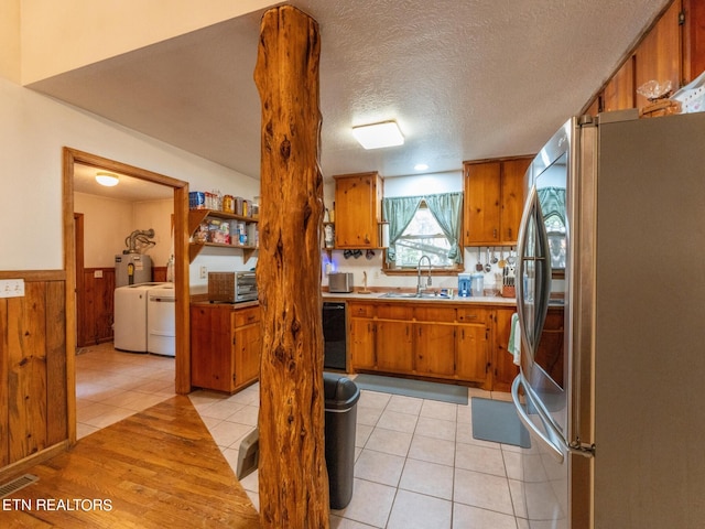 kitchen featuring light tile patterned flooring, stainless steel fridge, sink, washing machine and dryer, and a textured ceiling