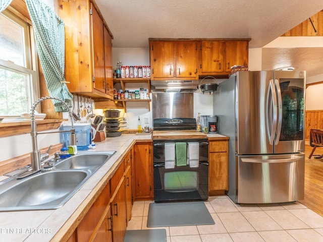 kitchen featuring wooden walls, stainless steel fridge, black stove, sink, and tile countertops