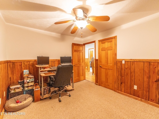 office featuring light carpet, wooden walls, and ceiling fan