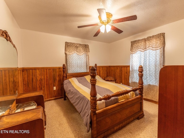 bedroom featuring light carpet, wooden walls, ceiling fan, and a textured ceiling