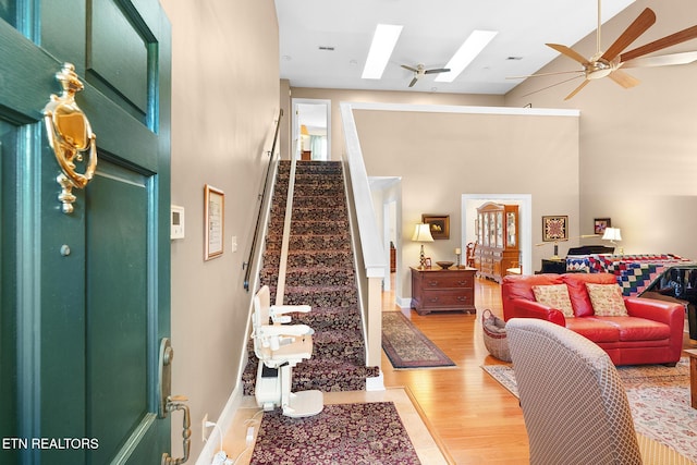 living room featuring a towering ceiling, a skylight, light wood-type flooring, and ceiling fan