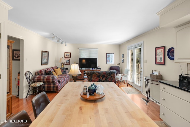 dining area with crown molding, track lighting, and light hardwood / wood-style flooring