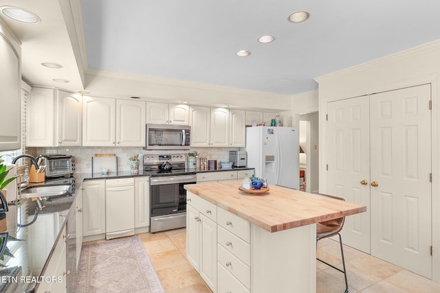 kitchen featuring wood counters, ornamental molding, a center island, white cabinets, and appliances with stainless steel finishes