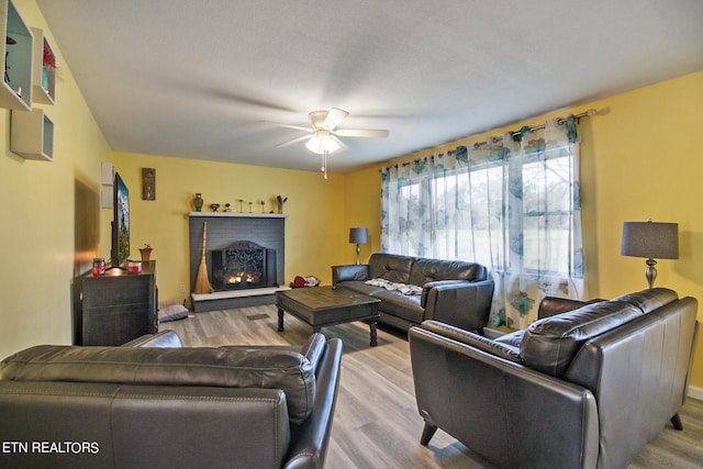 living room with light hardwood / wood-style flooring, ceiling fan, and a brick fireplace