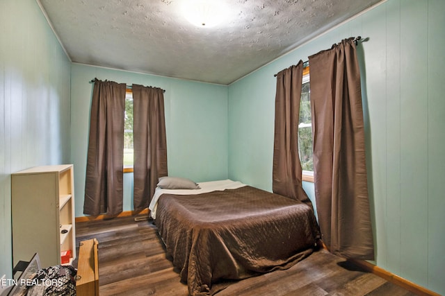 bedroom with a textured ceiling, dark hardwood / wood-style floors, and wood walls