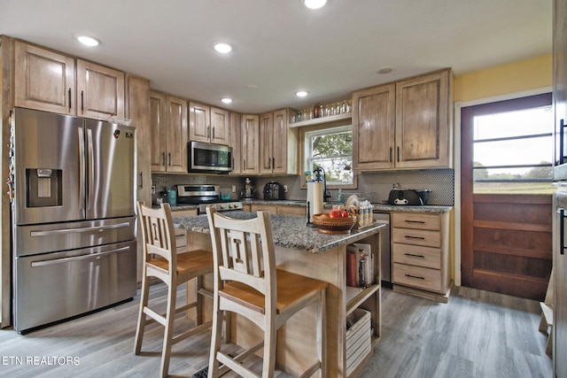 kitchen with a center island, stainless steel appliances, light hardwood / wood-style floors, and dark stone counters