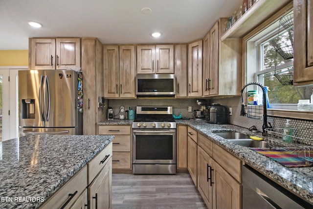 kitchen with light hardwood / wood-style floors, stainless steel appliances, sink, and dark stone counters