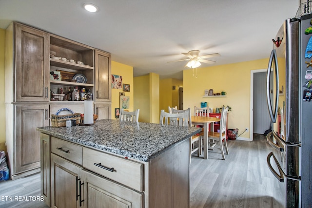 kitchen featuring stainless steel fridge, ceiling fan, a kitchen island, dark stone countertops, and light hardwood / wood-style floors