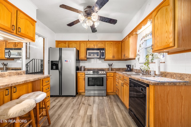 kitchen with a kitchen breakfast bar, sink, crown molding, light wood-type flooring, and appliances with stainless steel finishes