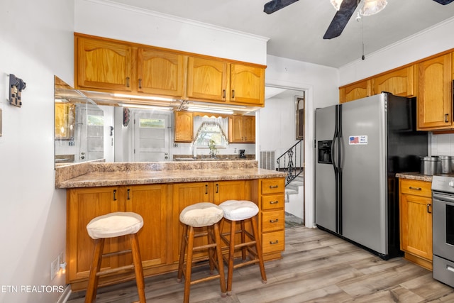 kitchen featuring light stone countertops, appliances with stainless steel finishes, a breakfast bar, ceiling fan, and light hardwood / wood-style flooring