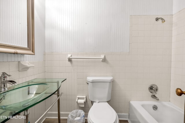 full bathroom featuring toilet, tiled shower / bath combo, sink, and tile walls